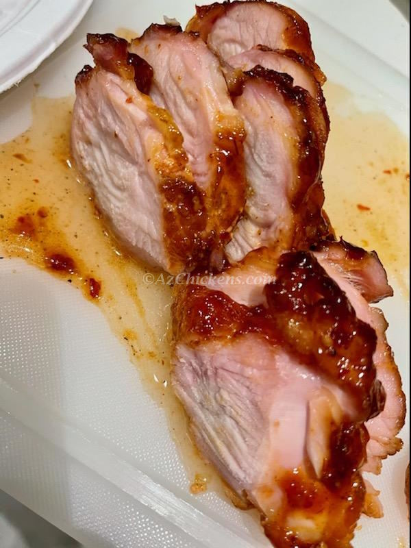 Sliced, succulent roasted chicken with a crispy exterior, glistening with sauce on a cutting board.